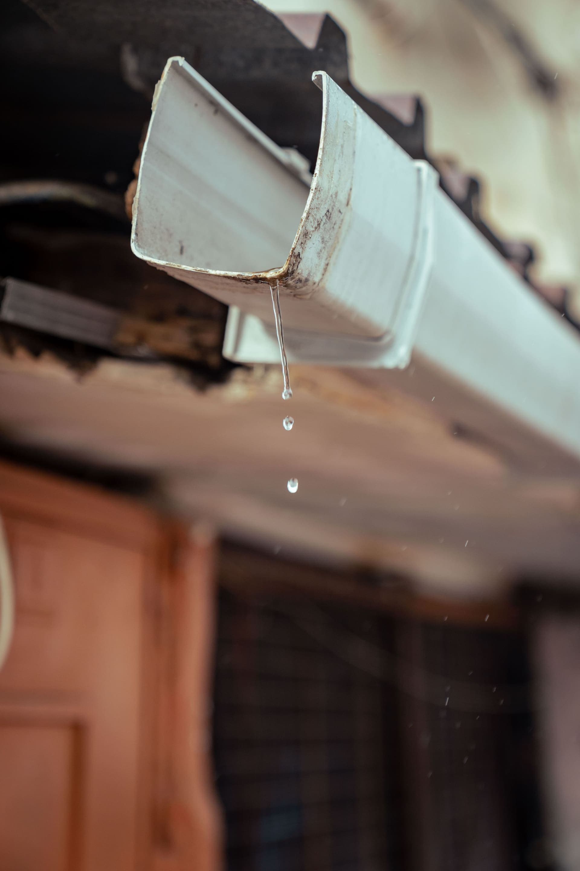 Rainwater dripping from the end of a white metal gutter at a roof edge