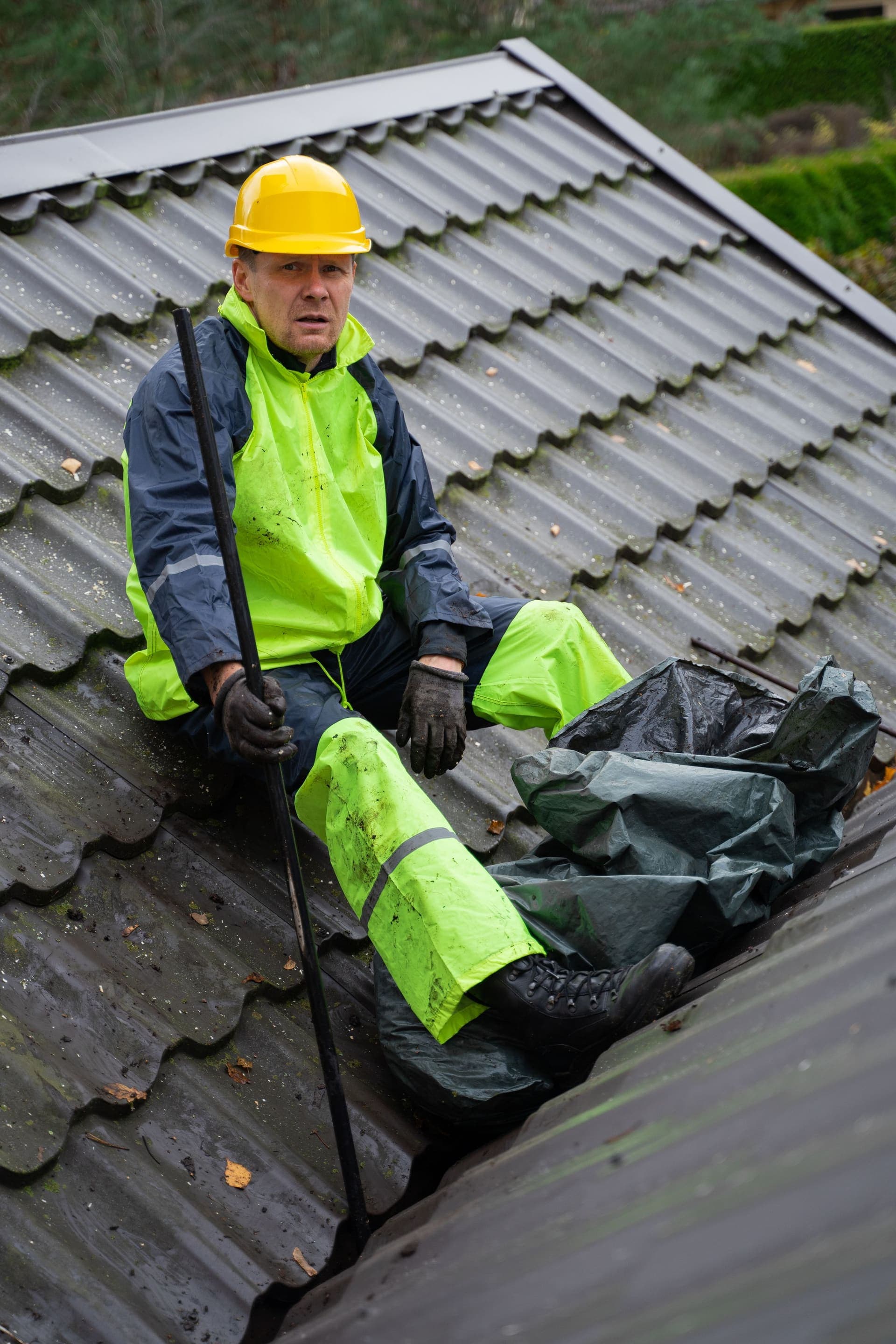 A roofer in wet-weather gear clearing moss and debris from a roof