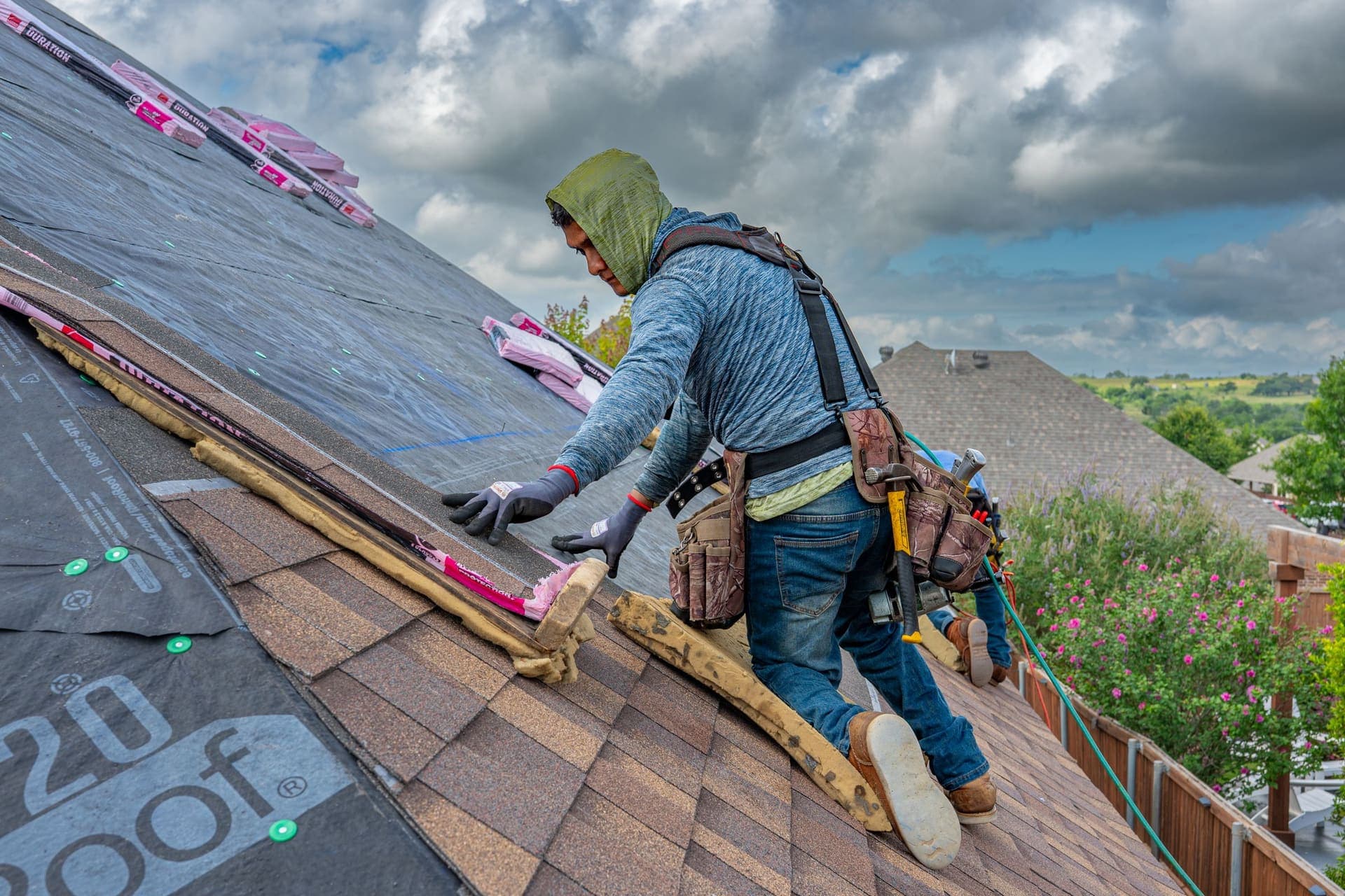 A roofer installing asphalt shingles on a roof under a cloudy sky